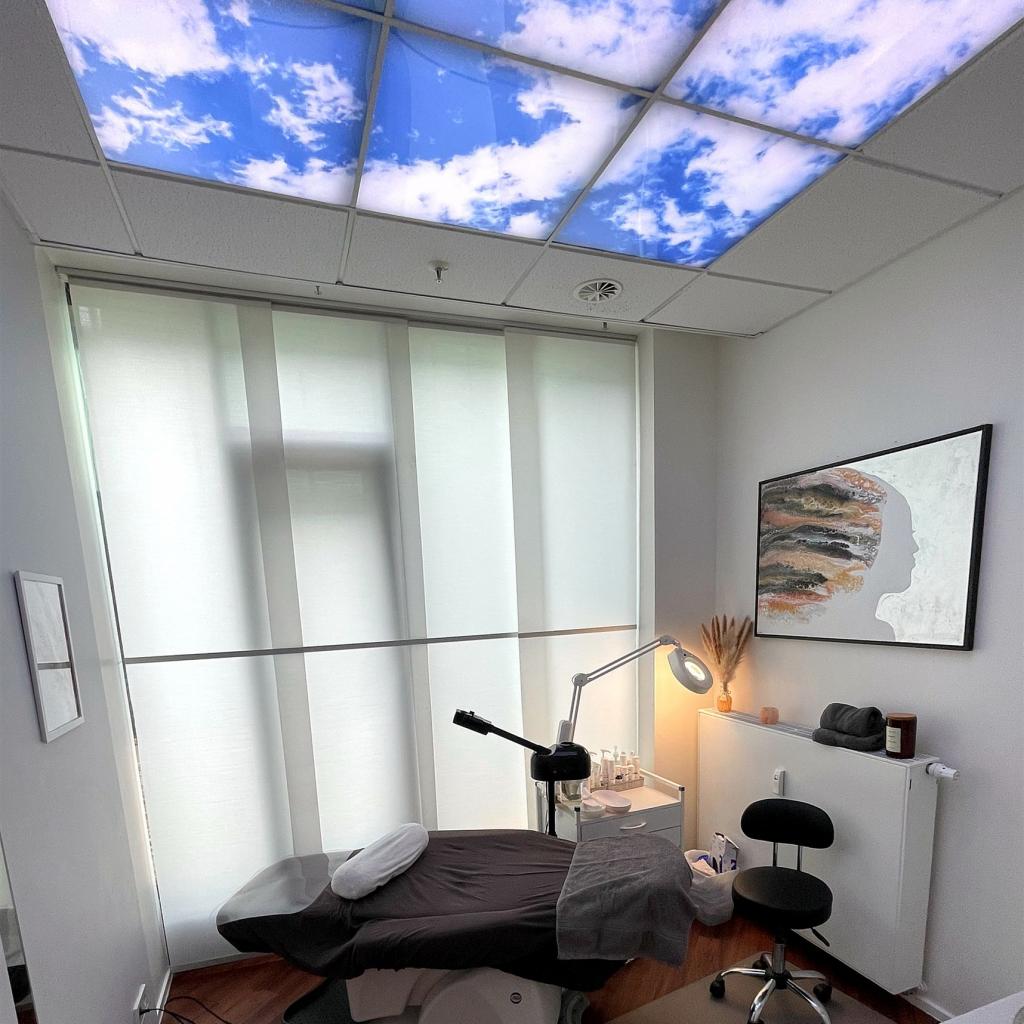Innenaufnahme eines modernen Raumes mit einer Decke, die einen blauen Himmel mit weißen Wolken darstellt, und einem Behandlungs-/Untersuchungstisch.