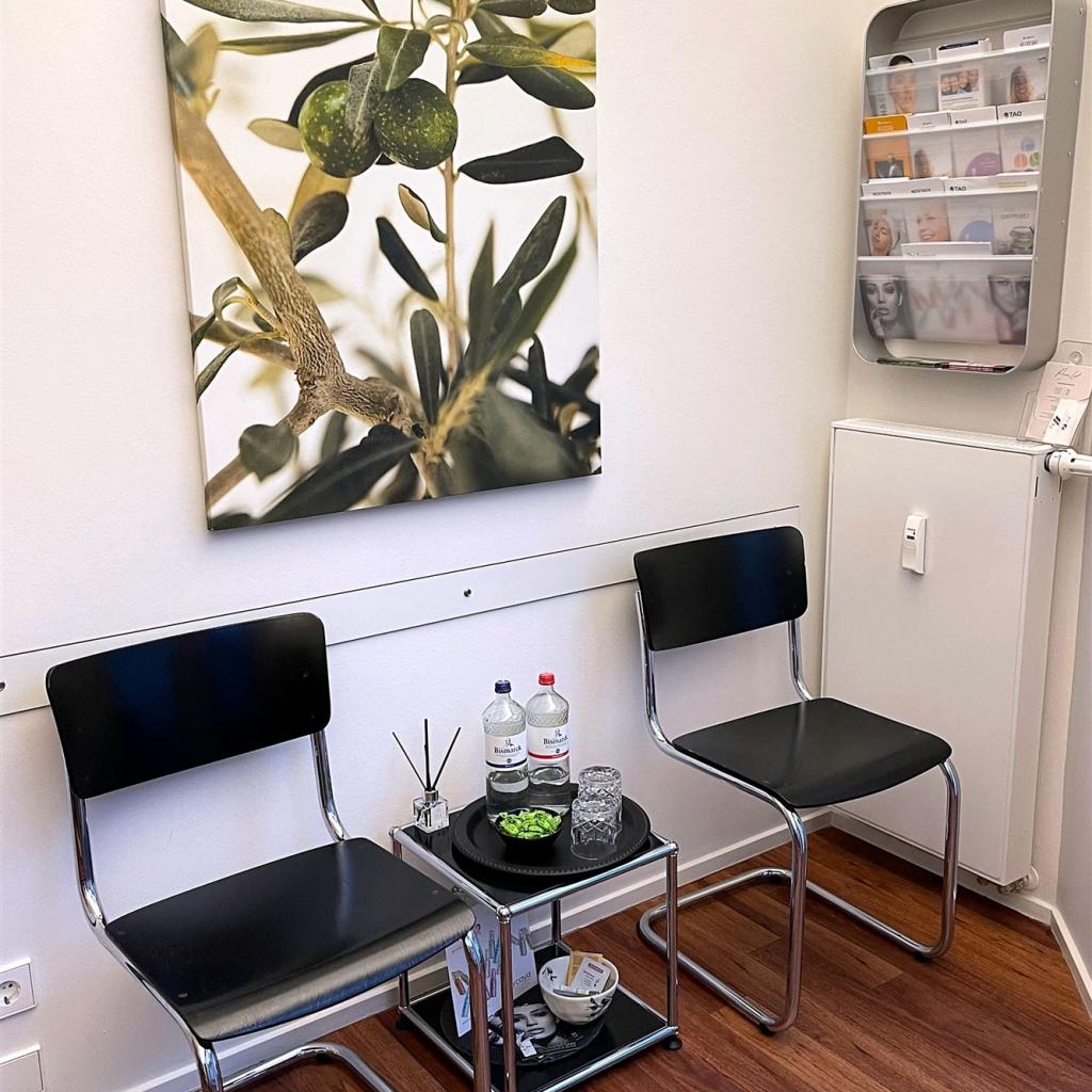 Ein moderner Wartebereich mit zwei Stühlen, einem Beistelltisch und einem großen botanischen Wandkunstwerk.
