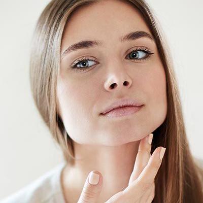 Porträt einer jungen Frau mit langen braunen Haaren, die ihre Hand am Hals positioniert.