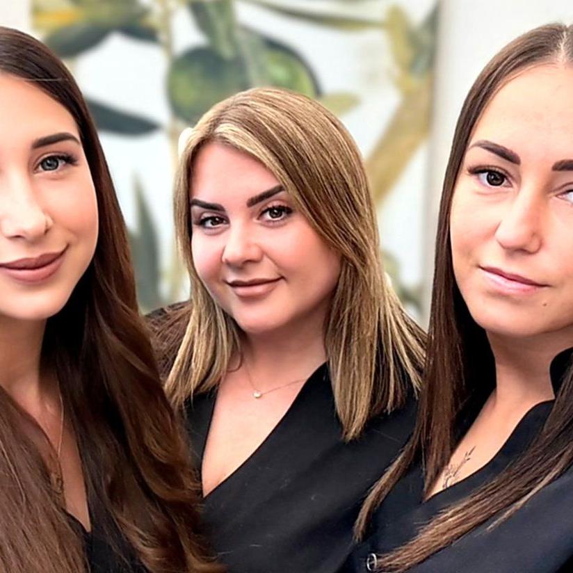 Drei junge Frauen mit langem braunem Haar posieren zusammen und blicken direkt in die Kamera.