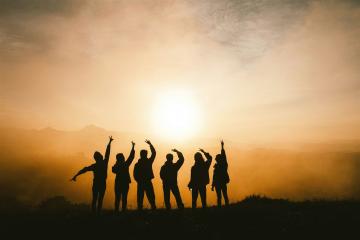 Silhouetten einer Gruppe von Menschen auf einem Hügel bei Sonnenuntergang.
